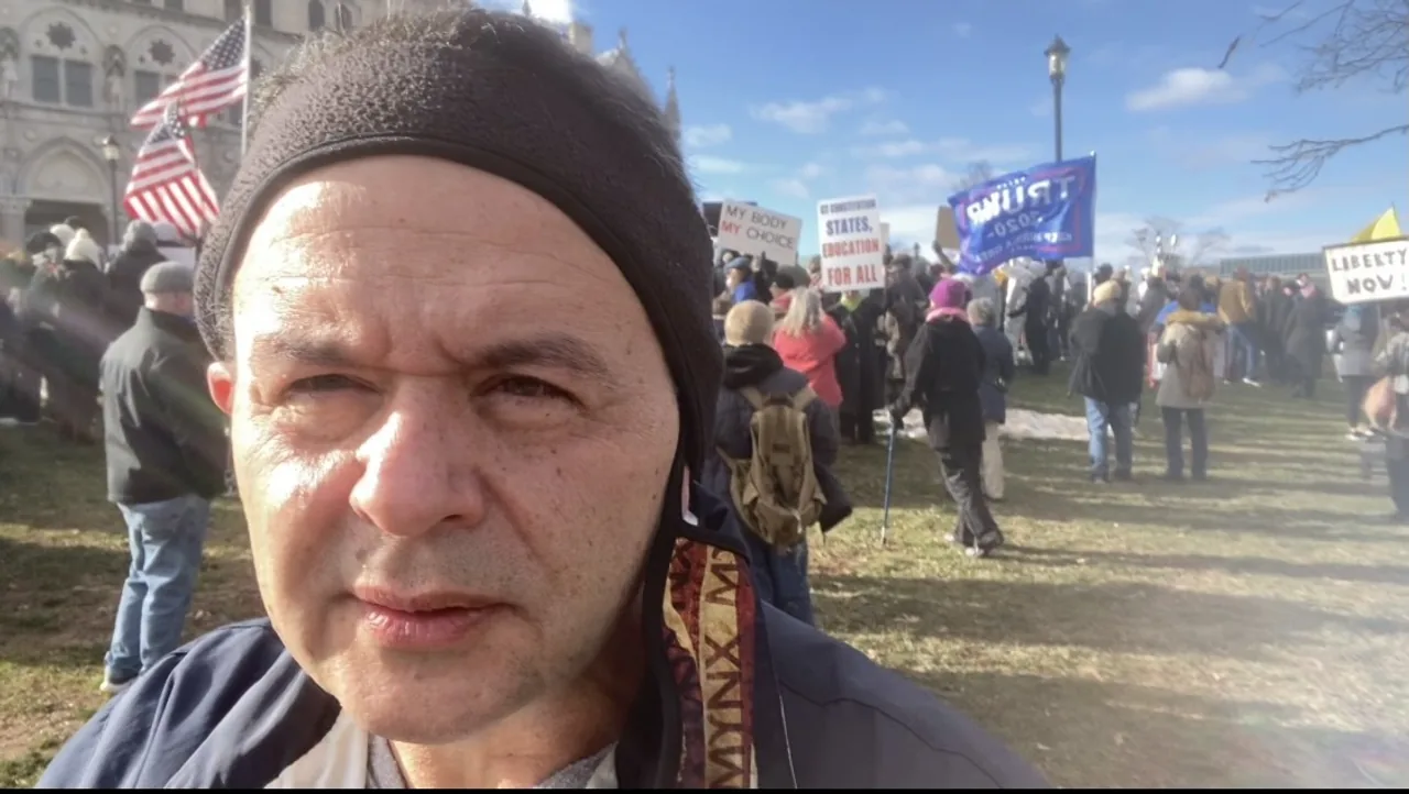 Dan Newmyer at a rally outside the Connecticut State Capitol, surrounded by American flags and demonstrators' signs